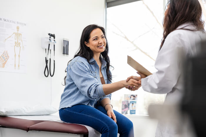 Woman in a doctor's office shaking hands with clinician.